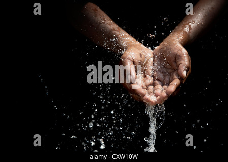 Indian mans cupped hands catching poured water against black background Stock Photo