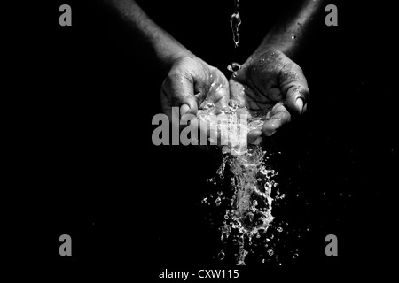 Indian mans cupped hands catching poured water against black background Stock Photo