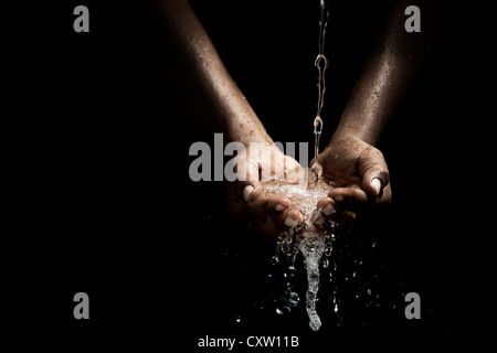 Indian mans cupped hands catching poured water against black background Stock Photo