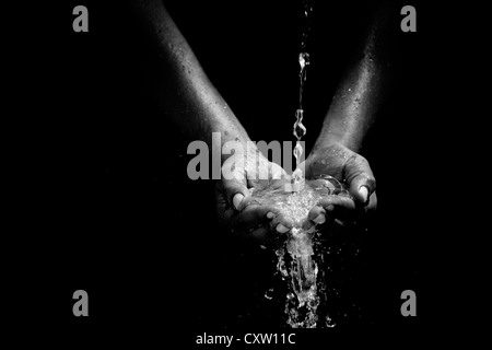 Indian mans cupped hands catching poured water against black background Stock Photo