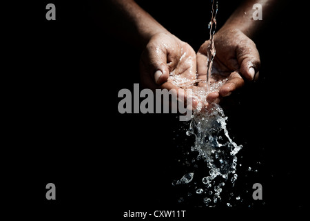 Indian mans cupped hands catching poured water against black background Stock Photo