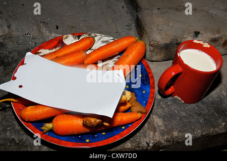 Cookies and milk for Santa Claus with carrots, in a rustic fireplace with a blank note Stock Photo