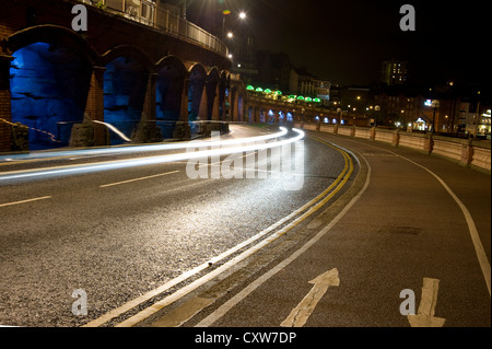 Car Light Trails Sweeping Up Local Road Late At Night. Empty Streets Abandoned Patrolled By A Lonely Police Car. Stock Photo
