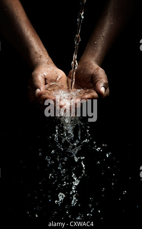 Indian mans cupped hands catching poured water against black background Stock Photo