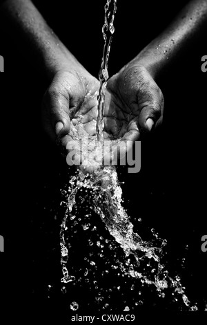 Indian mans cupped hands catching poured water against black background. Monochrome Stock Photo