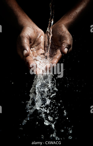 Indian mans cupped hands catching poured water against black background Stock Photo