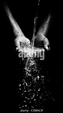 Indian mans cupped hands catching poured water against black background. Monochrome Stock Photo