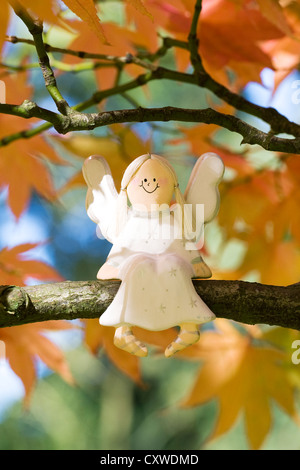 A wooden angel sitting on an Acer palmatum 'Amoenum' branch. Stock Photo