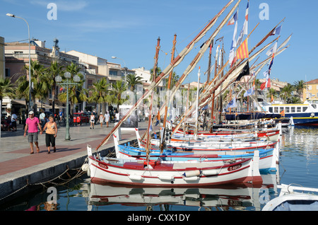 Tourists Walk Along Quayside next to Colourful Wooden Boats, known as Pointus, in the Port or Harbour of Sanary-sur-Mer Var Provence France Stock Photo