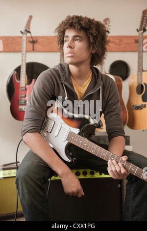 Mixed race teenager sitting with electric guitar Stock Photo