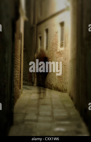 A shadowy figure stands under a streetlight in a dark Venice alley. Stock Photo