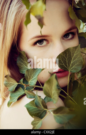 Close portrait of young woman partly covered by ivy looking into the camera Stock Photo