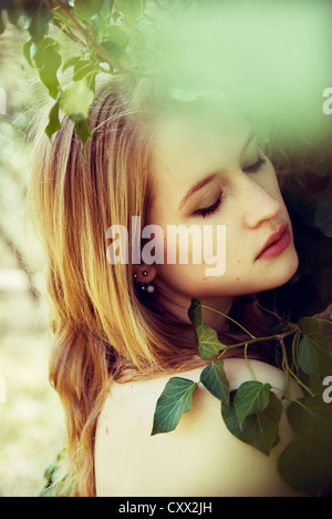 Portrait of young woman partly covered with ivy looking down to the side Stock Photo