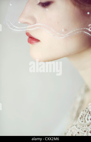 Close portrait of young woman looking down to the side with a bridal veil covering parts of her face Stock Photo