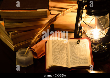 a bible surrunded by books in a lamp light Stock Photo