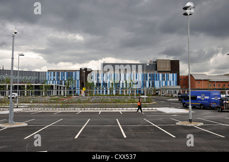 Hope Hospital, Salford. A construction worker in orange hi-vis vest uses mobile phone while walking across newly built car park. Stock Photo