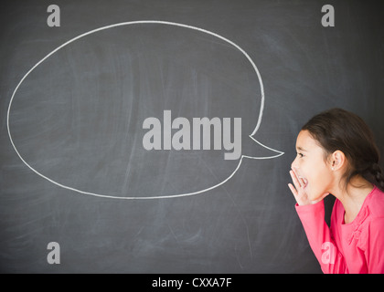 Mixed race girl standing by speech bubble on blackboard Stock Photo