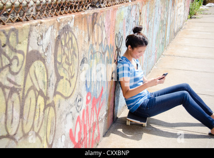 Asian woman sitting on skateboard using cell phone Stock Photo