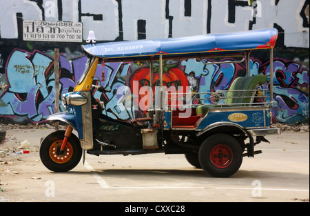 Tricycle motor rickshaw taxi in front of graffiti wall Bangkok, Thailand Stock Photo