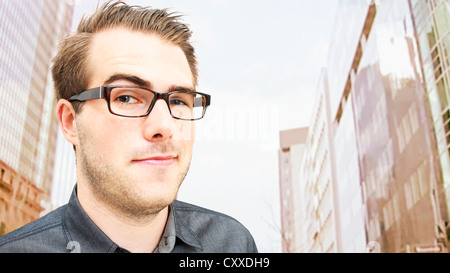 Portrait of a young man wearing glasses standing in front of high-rise buildings, sly glance Stock Photo