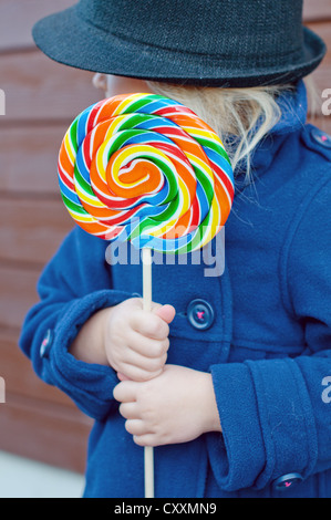 Girl holding big rainbow lollypop turning her face to the left Stock Photo