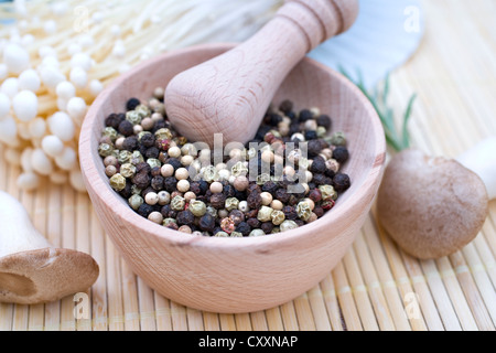 Wooden mortar with mixed pepper, enoki mushrooms and a king oyster mushroom Stock Photo