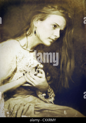 A woman , seated, in a vintage outfit and long hair, with painful expression and hands raised to her chest.