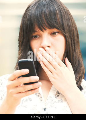 Young woman reading a text message, looking shocked Stock Photo