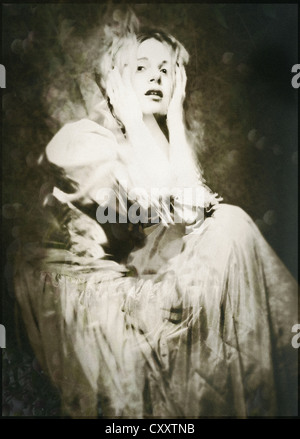A woman ina vintage gown, seated, with a dramatic expression and hands raised to her head.