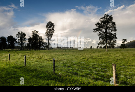 Electric fence and a large sheep pasture, against the backdrop of the Southern Alps, Fox Glacier, storm clouds with a rainbow Stock Photo