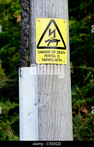 A bi-lingual sign in English and Welsh on a pole warning of the danger of electrocution from overhead power lines. Stock Photo