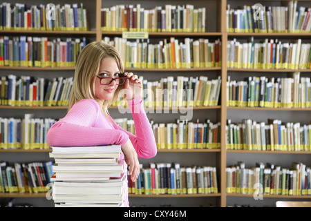 Female student wearing glasses with a stack of books in a university library Stock Photo