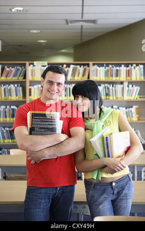 Male and female students holding books in a university library Stock Photo