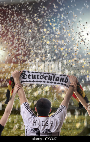 Football fan holding up a German supporters scarf, seen from behind, with confetti in a football stadium Stock Photo