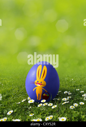 Blue Easter egg painted with an Easter bunny on a meadow with daisies Stock Photo