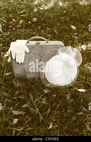 an old, blue leather case with white gloves and white hat on a meadow Stock Photo