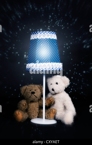 two teddy bears are sitting under an old vintage lamp Stock Photo