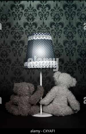 two teddy bears are sitting under an old vintage lamp Stock Photo