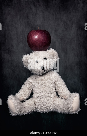 a white teddy bear with a red apple on the head Stock Photo