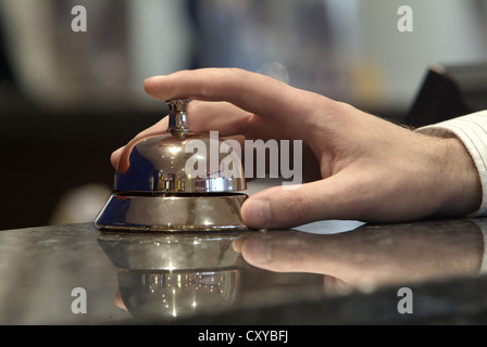 Hand resting on a hotel reception bell Stock Photo