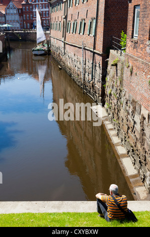 Senior citizen sitting on the bank of the Schwinge river looking towards the old town of Stade, Lower Saxony Stock Photo