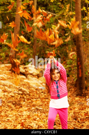 Image of small cute female child enjoying autumn nature, little pretty girl playing game in fall park, adorable sweet kid Stock Photo