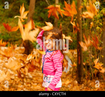 Photo of little cute girl playing in autumn park, adorable sweet kid throwing up old dry foliage, cheerful small female child Stock Photo