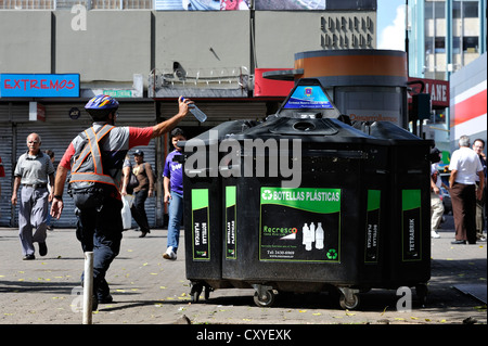 Man throwing a plastic bottle into a container for recyclables, waste separation and recycling, pedestrian zone of San José Stock Photo