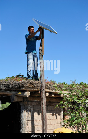 Young man mountain solar cells on the roof of a simple hut of a smallholder's farm, Gran Chaco, Santiago del Estero Province Stock Photo