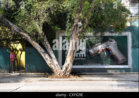 Billboard, advertisement for a gun, on the left an armed guard standing in front of a door, Guatemala City, Guatemala Stock Photo