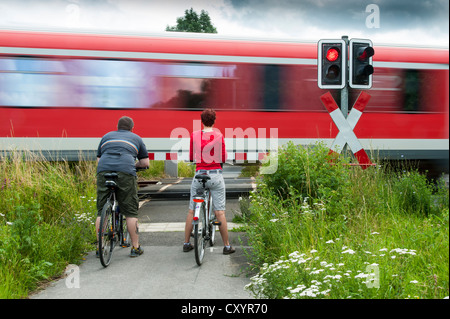 A man and a woman with bicycles standing at a closed railway crossing, Grevenbroich, North Rhine-Westphalia Stock Photo