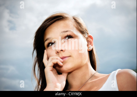 Girl, 14 years, looking up thoughtfully, in front of cloudy sky Stock Photo