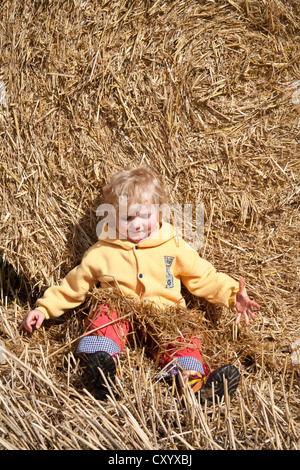 Little girl leaning against a straw bale playing with straw, Saxony Stock Photo