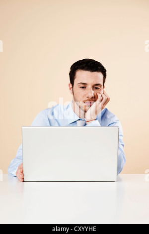 Young man sitting in front of his laptop computer, thoughtful Stock Photo